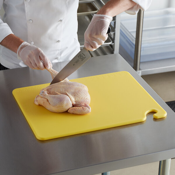 A chef using a San Jamar yellow cutting board to cut a chicken.