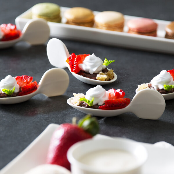 A close up of a 10 Strawberry Street Whittier white porcelain spoon with a dessert of strawberries and whipped cream.