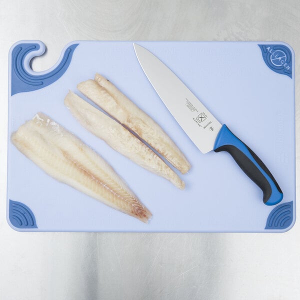 A blue San Jamar cutting board with fish on it and a knife next to fish.