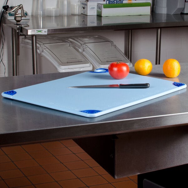 A San Jamar blue cutting board with a knife and a tomato on it.