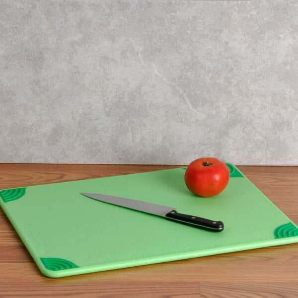 A green San Jamar cutting board with a tomato and a knife.