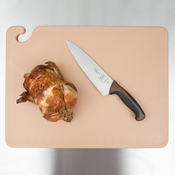 A knife and a chicken on a San Jamar brown cutting board.