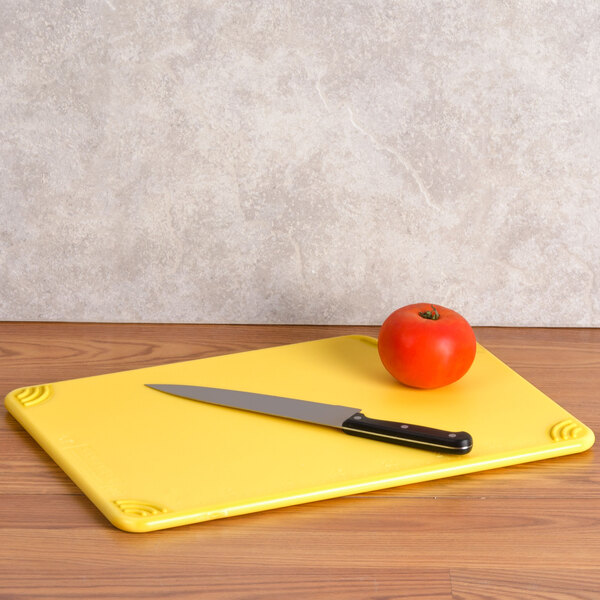A San Jamar yellow cutting board with a knife cutting a tomato.