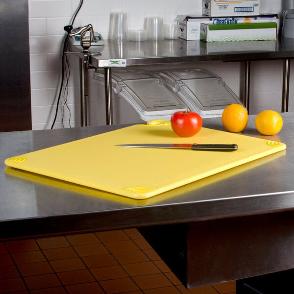 A yellow San Jamar Saf-T-Grip cutting board on a counter with a knife and fruit.