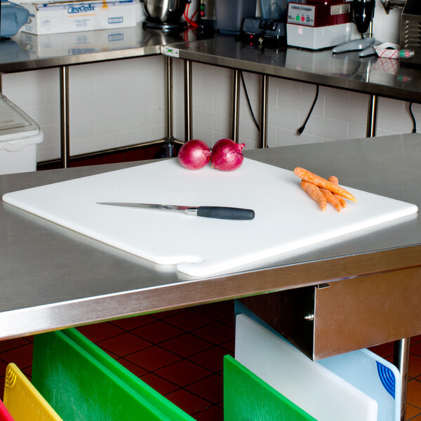 A San Jamar white cutting board on a kitchen counter with a knife and onions.