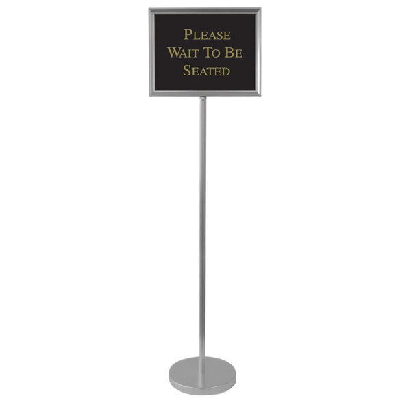 A silver metal Aarco hostess/teller sign with a black sign and gold text on it.