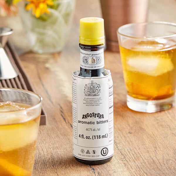 A bottle of Angostura Aromatic Bitters on a table with a glass of ice and a drink.