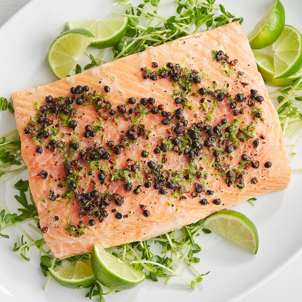 A piece of salmon with Regal Juniper Berries, limes, and greens on a plate.