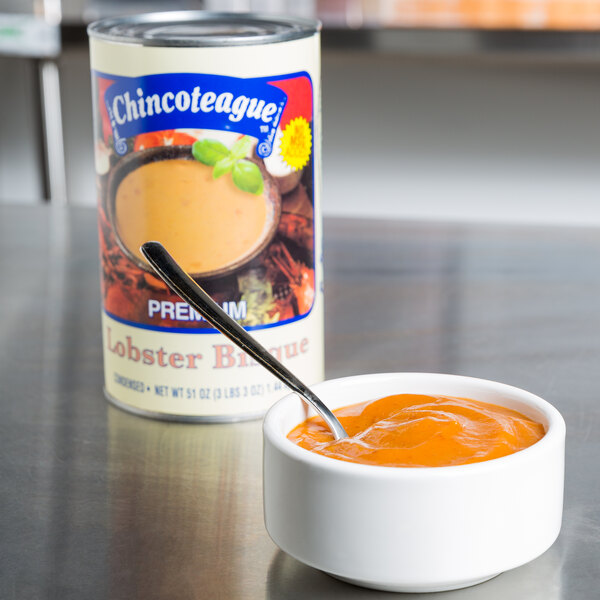 A bowl of Chincoteague Lobster Bisque with a spoon in it next to a can of Chincoteague Lobster Bisque.
