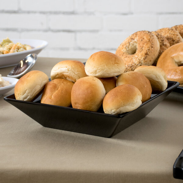 A black Siciliano square melamine bowl filled with bread on a table