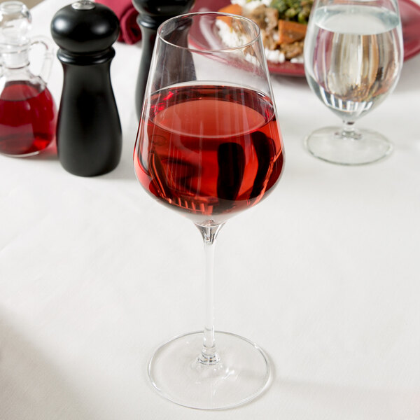 A Stolzle Quatrophil wine glass filled with red wine on a table.