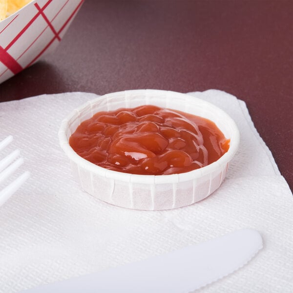 A Solo white paper souffle cup filled with red sauce on a white surface.