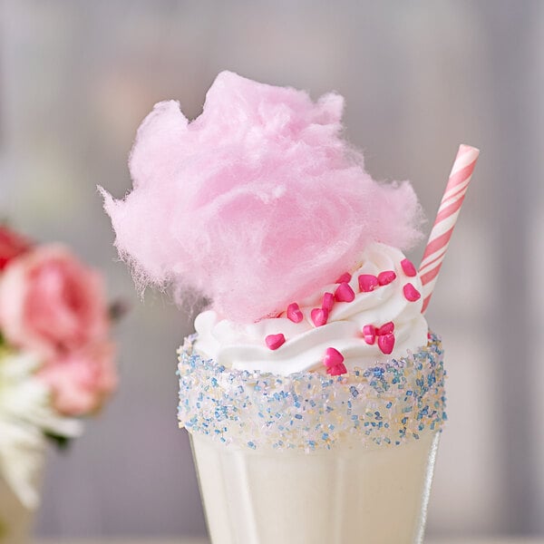 A close up of a milkshake topped with pink cotton candy and sprinkles.