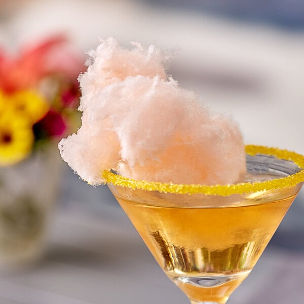 A glass of yellow liquid with a yellow rim and cotton candy with a Great Western cotton candy carton on the table.