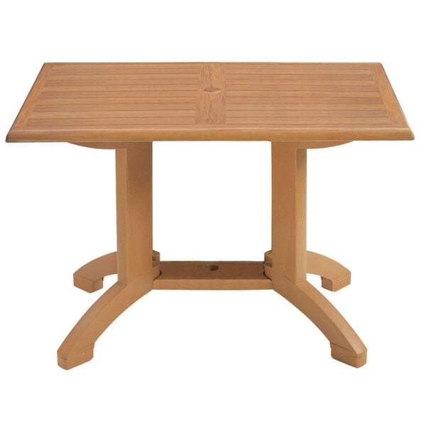 A Grosfillex rectangular teak pedestal table with a hole in the middle.