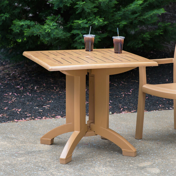 A Grosfillex Teak Decor pedestal table with two cups of liquid on it.