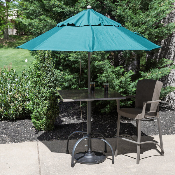 A table and chairs under a turquoise Grosfillex umbrella with a metal pole.