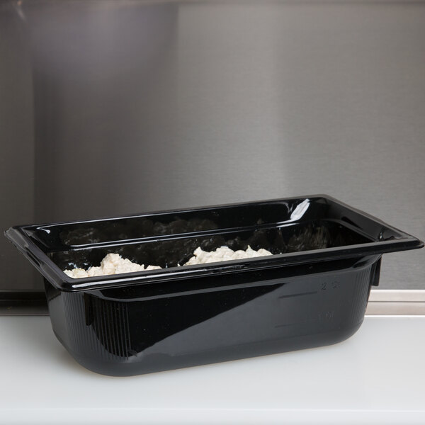 A Vollrath black polycarbonate food pan with food inside.