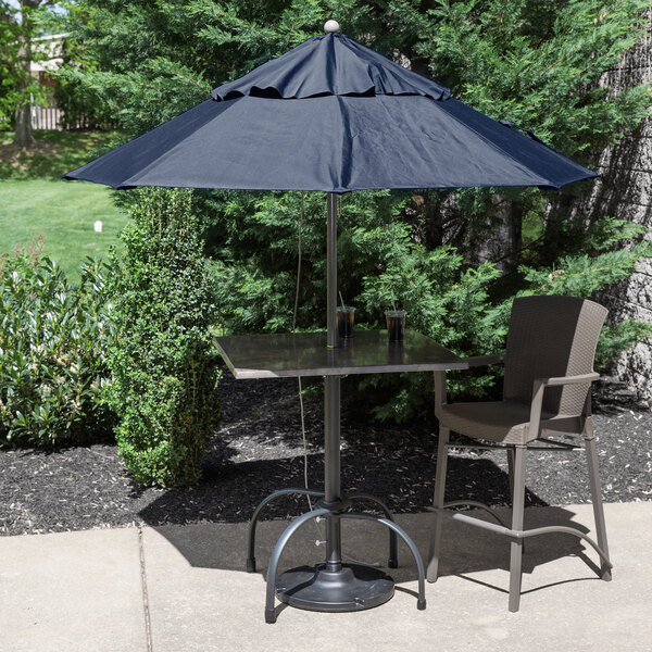 A table with a blue Grosfillex Windmaster umbrella with a metal pole on an outdoor patio.
