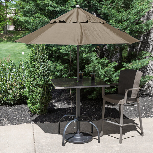 A table with a Grosfillex taupe umbrella on it and chairs.