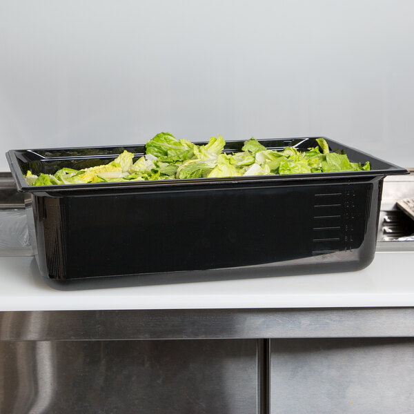 A Vollrath black polycarbonate food pan with lettuce in it on a counter.