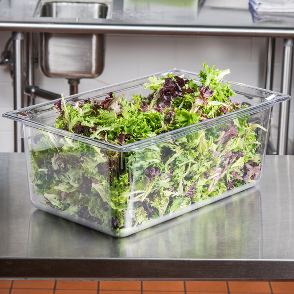A Vollrath clear polycarbonate food pan filled with lettuce on a counter.