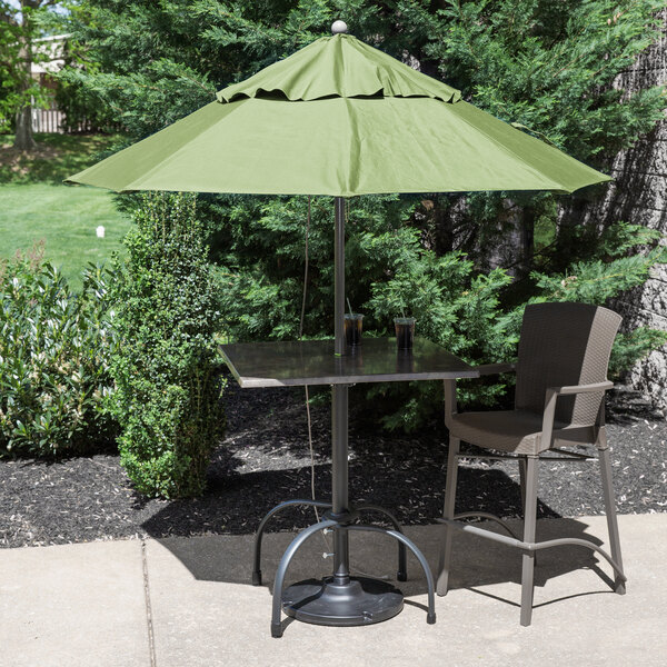 A table with a metal base and two chairs under a green Grosfillex umbrella.