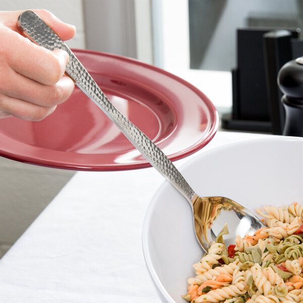 A person using an American Metalcraft hammered stainless steel spoon to serve pasta.
