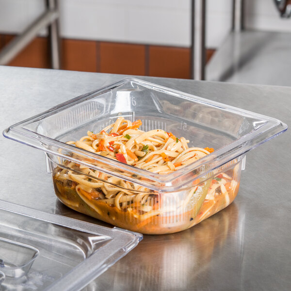 A clear plastic Vollrath food pan with noodles and vegetables in it on a counter.