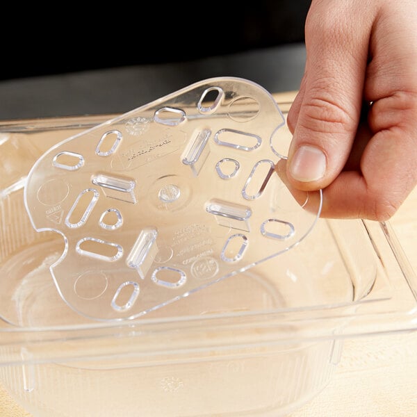 A hand holding a Vollrath clear polycarbonate drain tray over a counter.