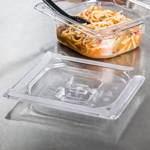 A Vollrath clear plastic slotted cover on a container with food and a spoon inside.
