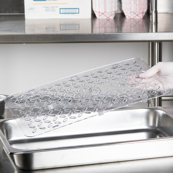 A gloved hand holding a clear plastic Vollrath drain tray.