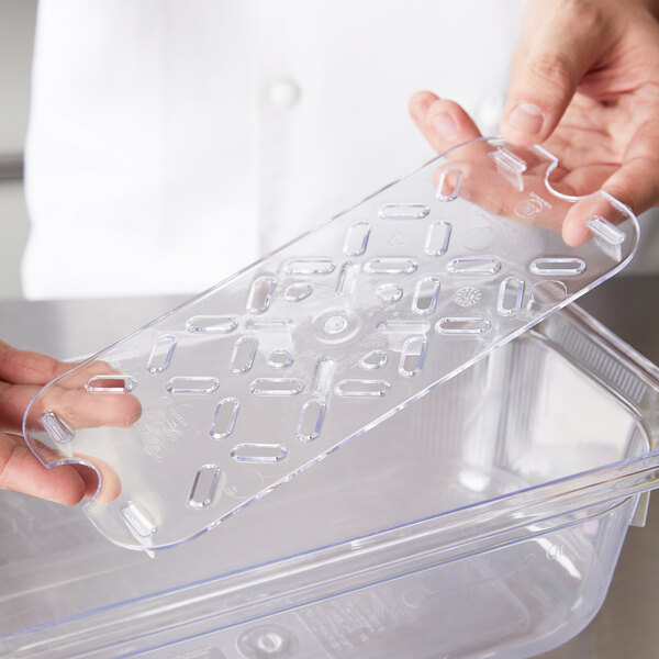 A person holding a Vollrath clear polycarbonate drain tray on a counter.