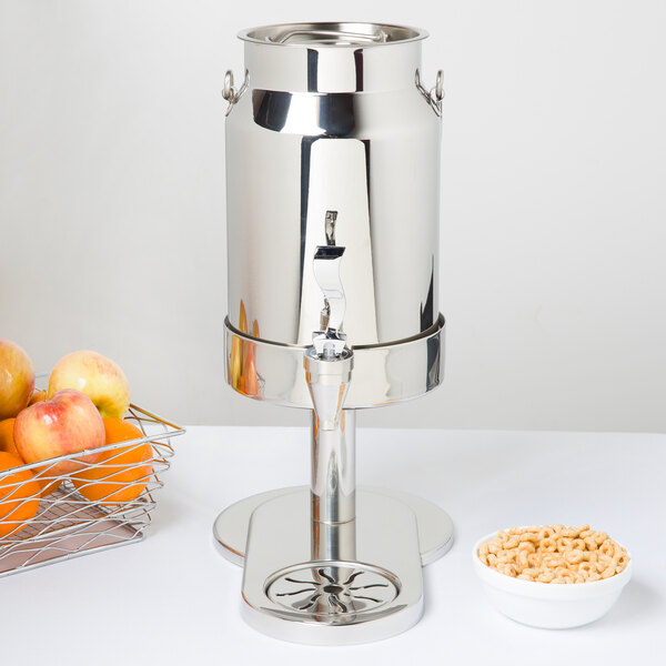 A Vollrath stainless steel beverage dispenser with a bowl of fruit inside.
