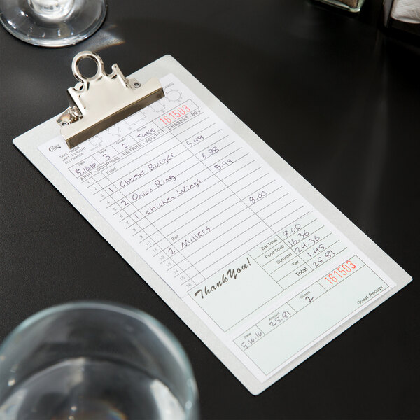 A clipboard with a green and white carbonless receipt on it sitting on a table.