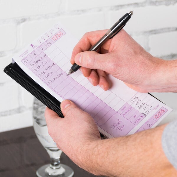 A hand holding a black pen and writing on a purple and white Choice guest check.