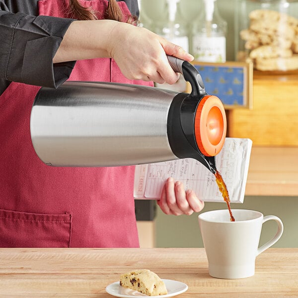 A woman pouring decaf coffee from a Curtis stainless steel coffee server into a white mug.