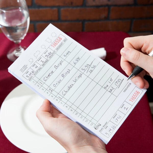 A hand holding a pen and writing on a green and white Choice guest check.