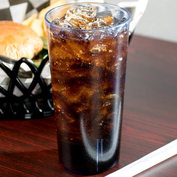 A Cambro slate blue plastic tumbler filled with soda and ice on a table with a burger in a black and white basket.