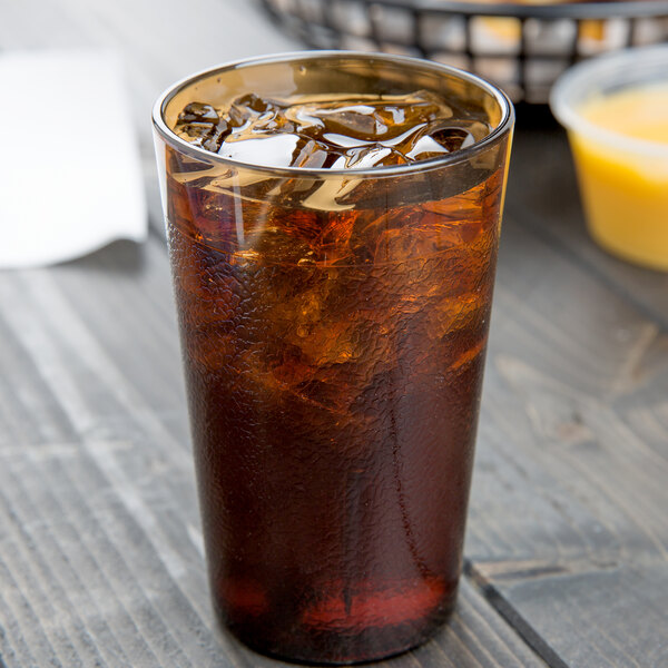A Cambro amber plastic tumbler filled with brown liquid and ice with a straw.
