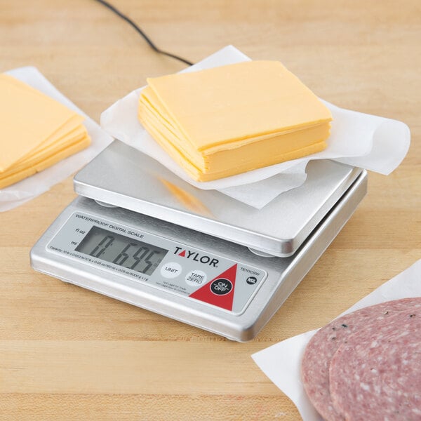 A Taylor digital portion scale with cheese and meat on a white plate.