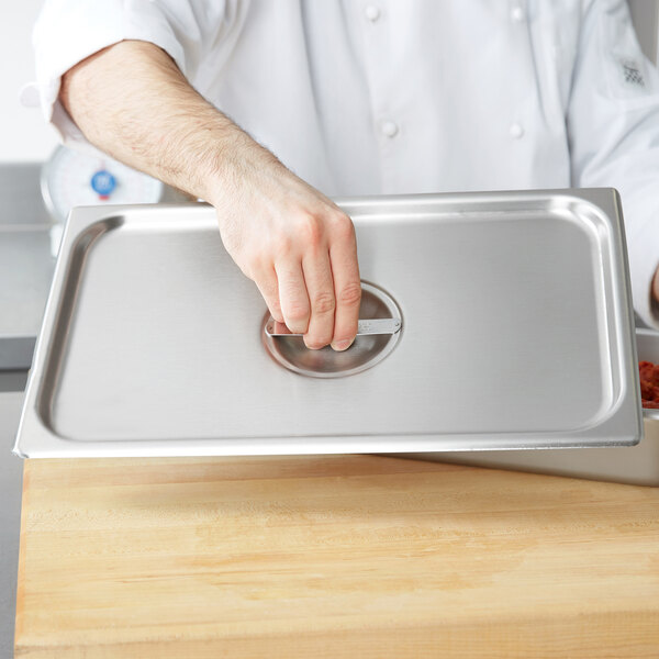 A chef holding a Vollrath stainless steel deli pan cover over a stainless steel pan.