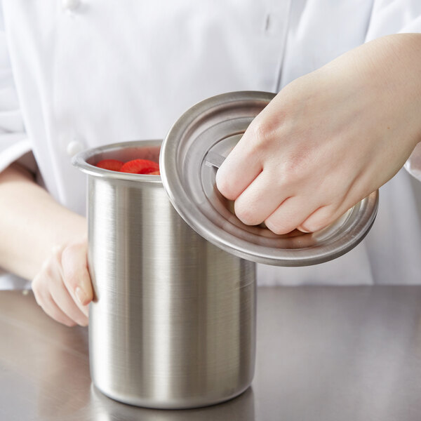 A hand putting a Vollrath stainless steel container into a silver pot.