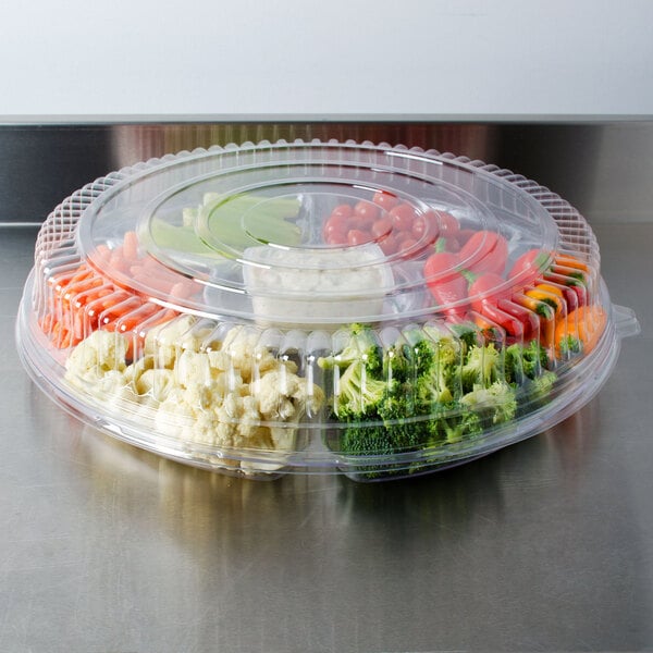 A Fineline clear plastic container with a clear low dome lid filled with broccoli and other vegetables.