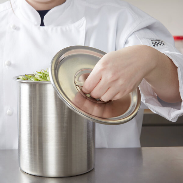 A chef using a Vollrath stainless steel bain marie cover to put food in a container.