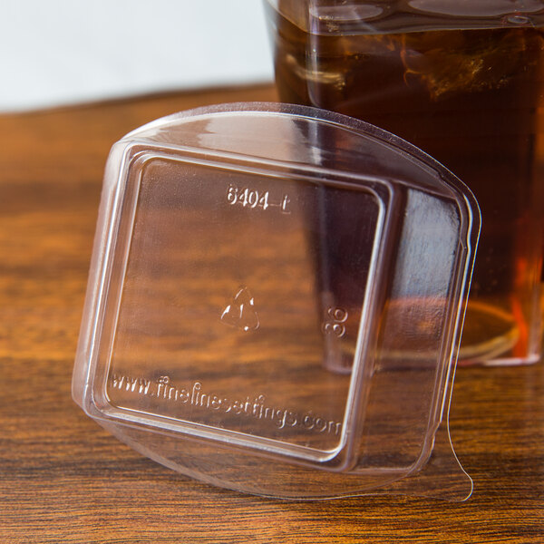 A Fineline clear plastic container with a clear dome lid next to a glass of liquid.