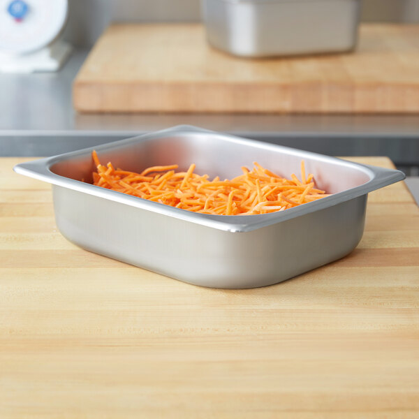 A Vollrath stainless steel deli pan with shredded carrots on a white counter.
