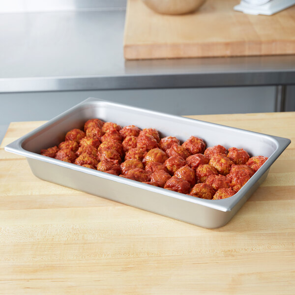 A stainless steel Vollrath deli pan filled with meatballs in sauce on a table.