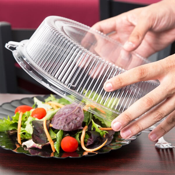 A person holding a Fineline clear plastic lid over a salad in a plastic container.