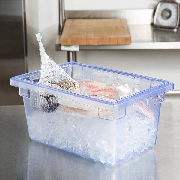 A Carlisle blue plastic food storage box filled with ice and fish on a professional kitchen counter.